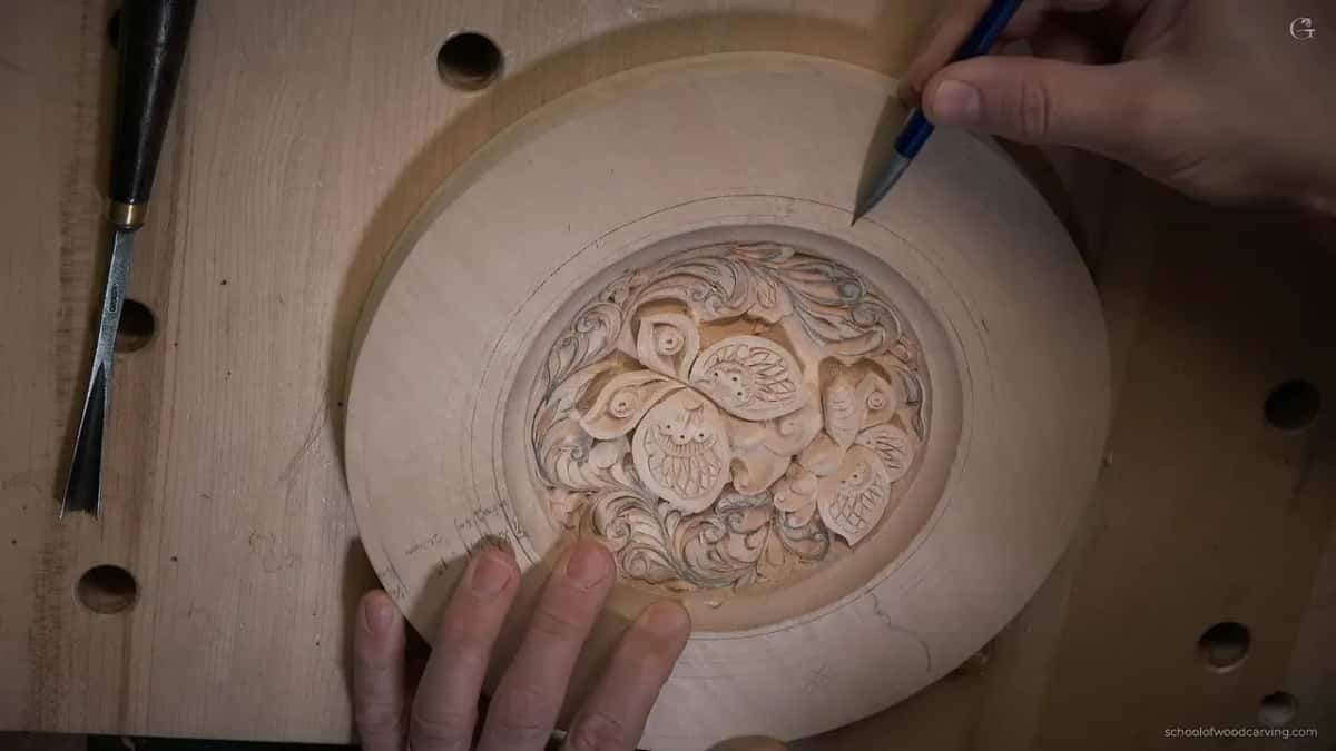Pencil point just within the carved plate's rim, both hands on the work.