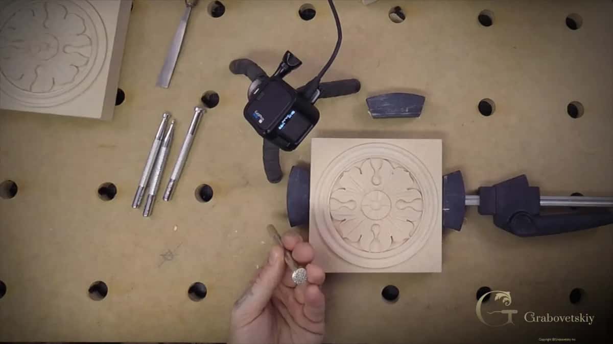 Hand raises a round leather punch next to a carved rosette clamped on the bench
