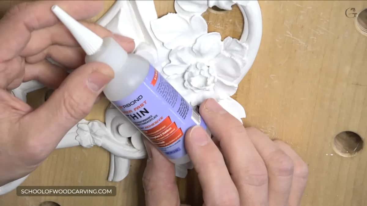 Starbond thin cyanoacrylate held above a primed white carving of flowers and scrolls