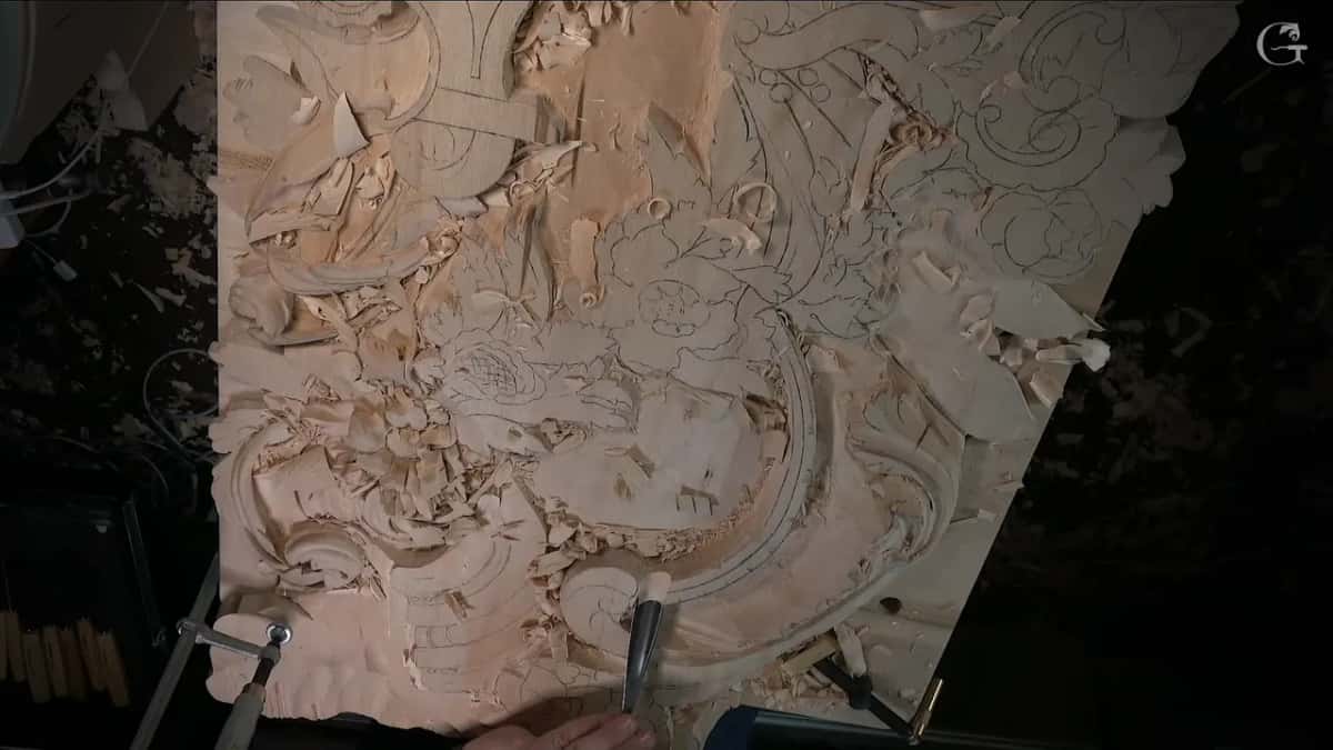 Overhead view with one hand holding a gouge near the curve and the design drawn across the board