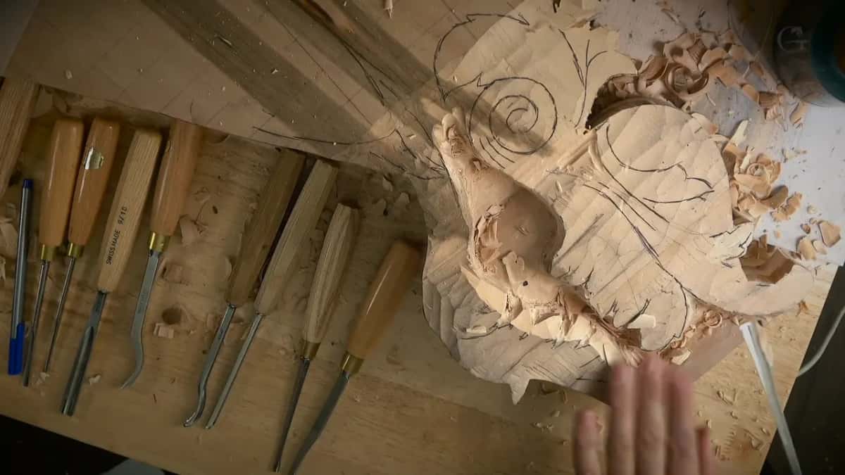 Gouges laid out in a row beside a large scroll still covered in pencil lines