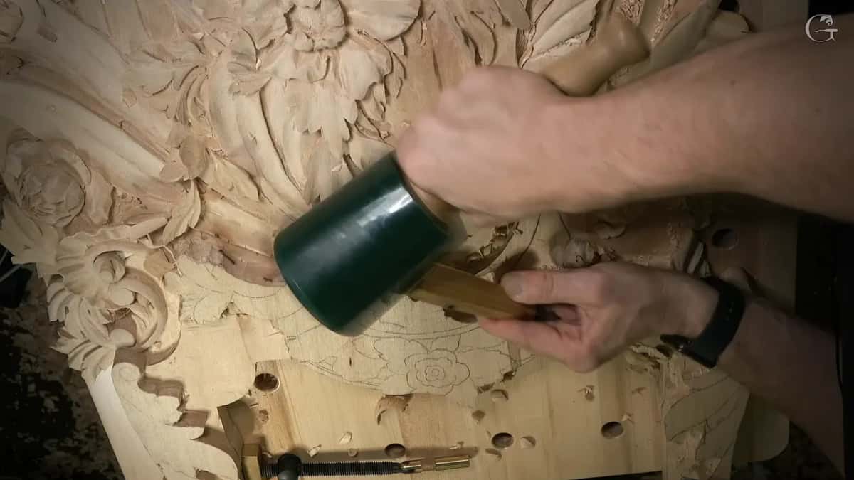 Green mallet comes down on a gouge handle while the other hand holds the blade to the panel