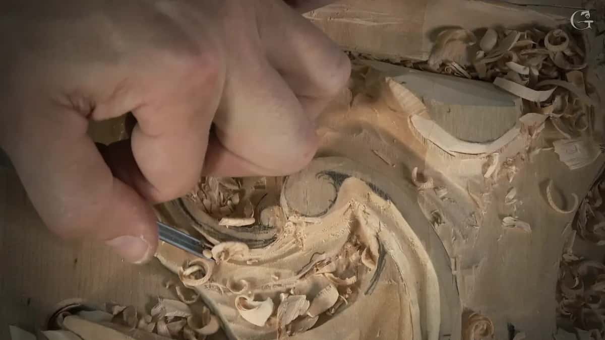 Knuckles bent over the scroll, tool tip low