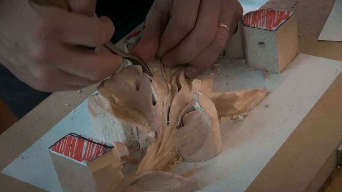 Both hands guide a bent gouge into the upper right lobe while the red-topped blocks stand at two corners