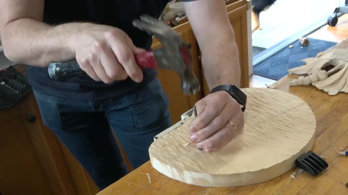 Red handled claw hammer coming down on a nail held to a round board