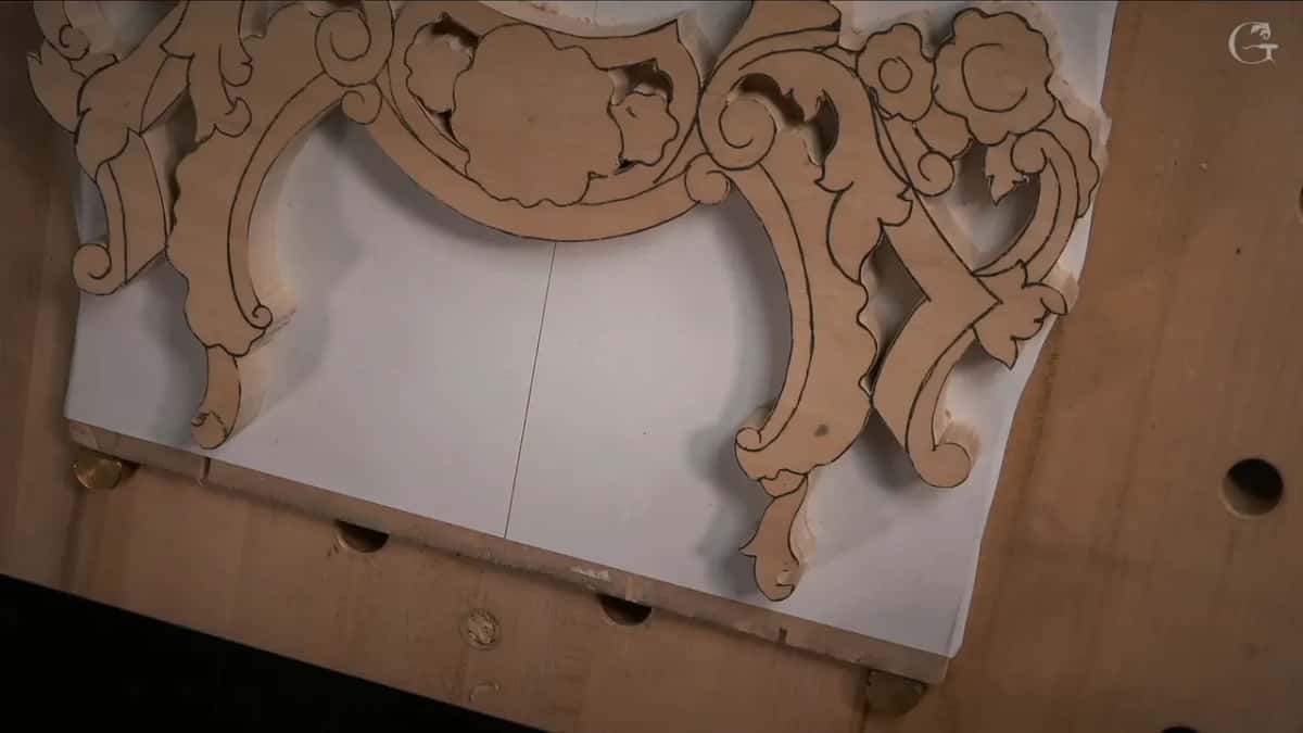 Sawn floral molding blank lying on a white board, with a brass peg at one corner.