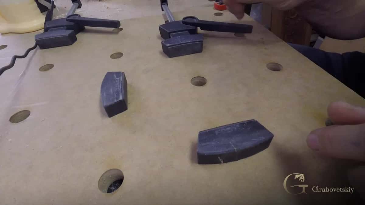 Two lever clamps and a pair of dark stops on a drilled MDF board, a hand at the right.