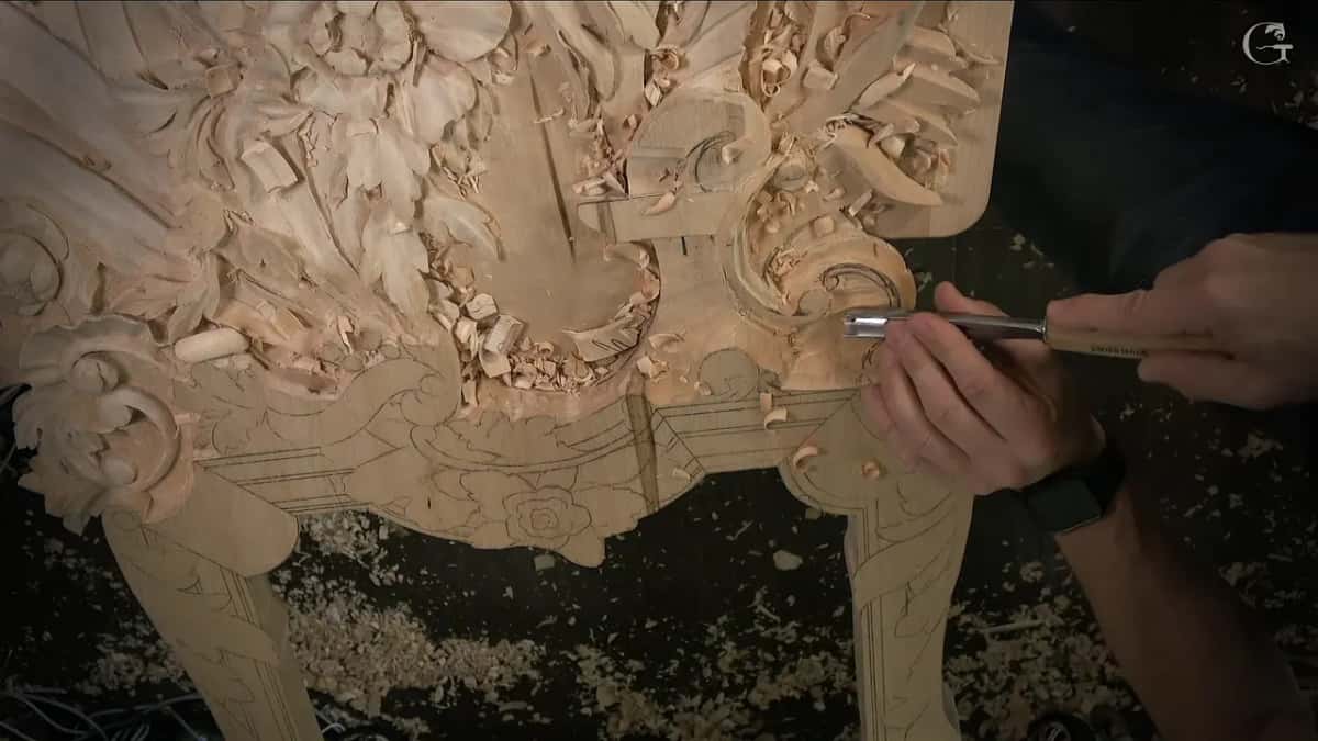 Both hands push a gouge flat across the lowered ground near the volute