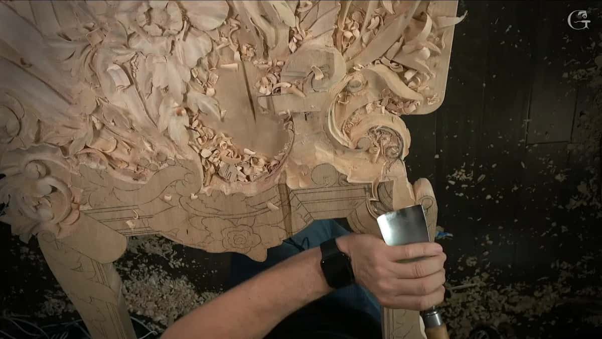 A gouge almost as wide as a hand, held upright at the edge of the carved panel