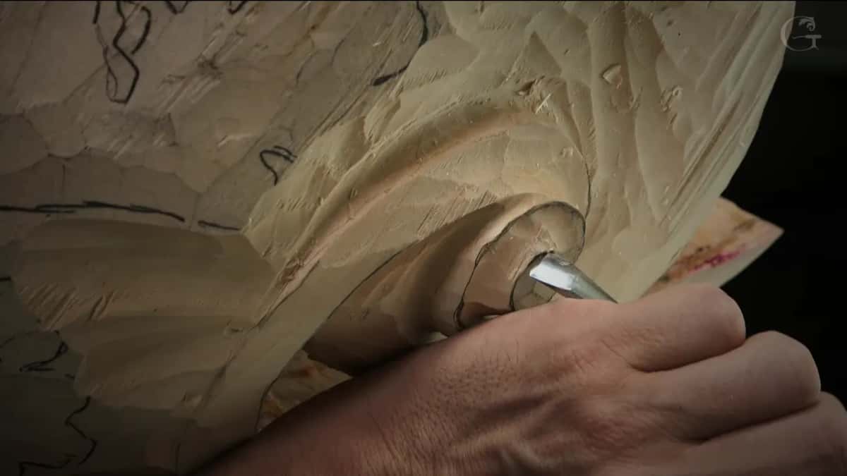 Hand holding a gouge down in a deep hollow of a leaf, the wood around it rough from earlier passes