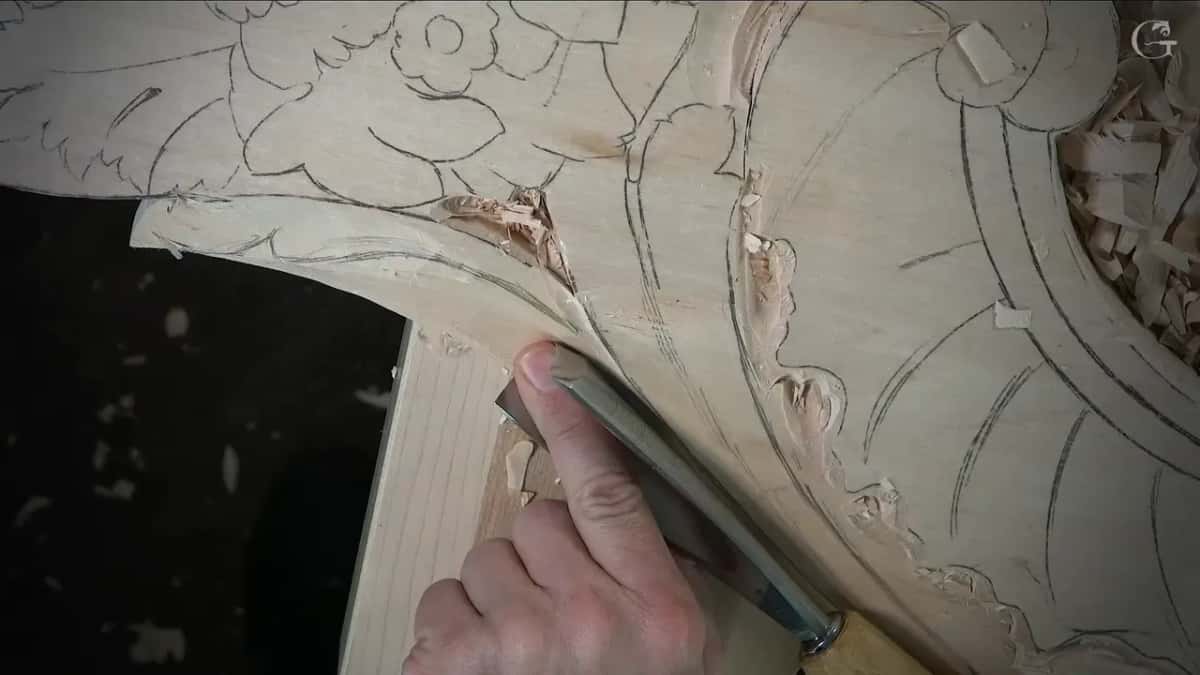 Large gouge held low at the curved border of a drawn flower panel, chips caught in the corner