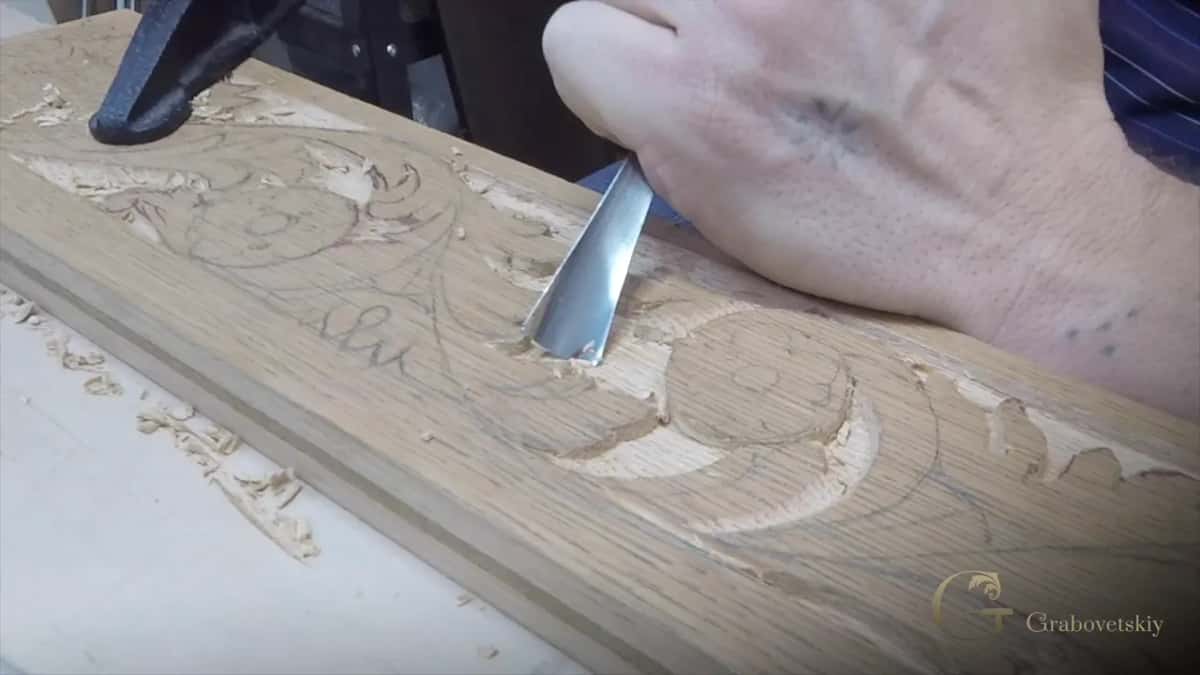 Wide gouge laid on one edge inside a carved scroll on a long apron board