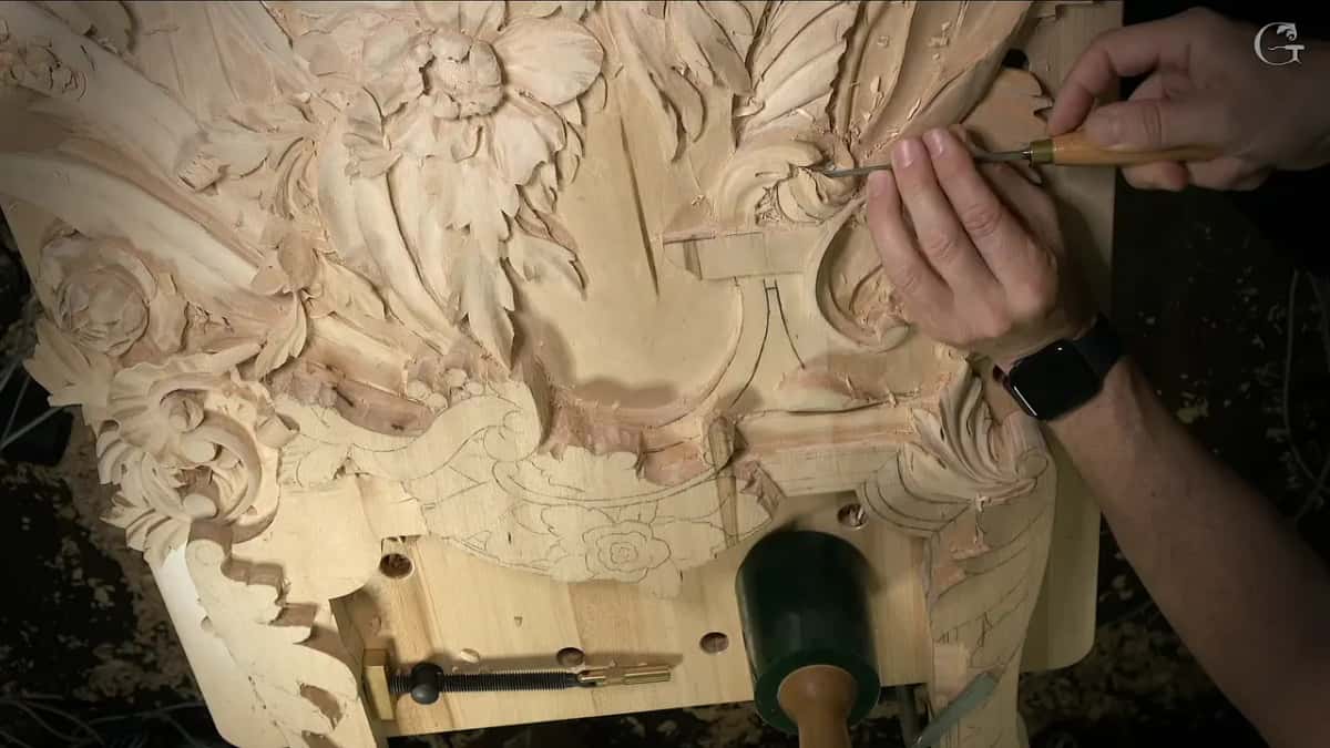 Both hands work a tool high on the panel while a green mallet stands on the bench below