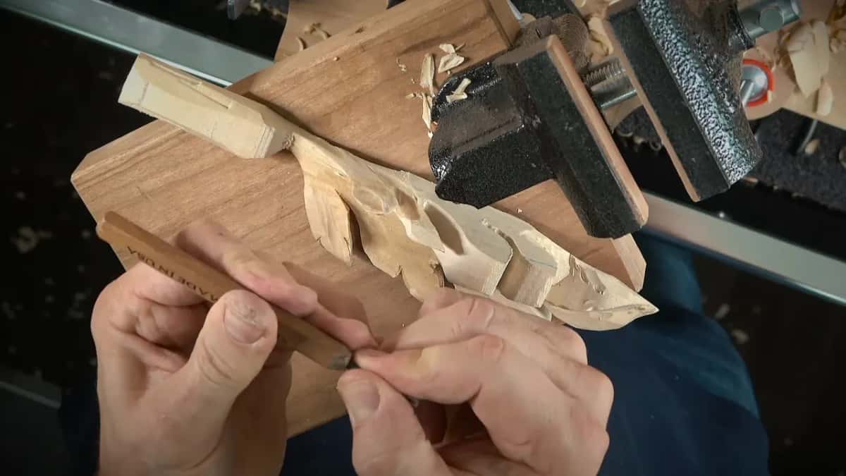 Both hands hold a slim dark handle beside a bench vise