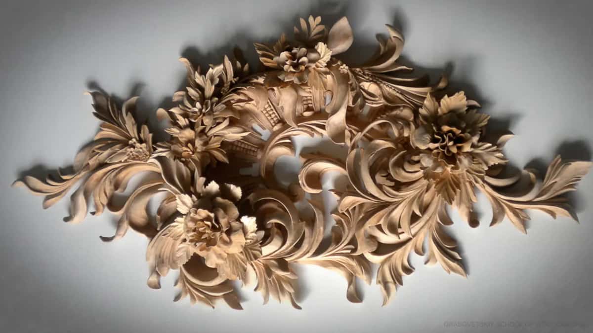 Carved flowers, leaves and stems hang in one big cluster on a gray wall