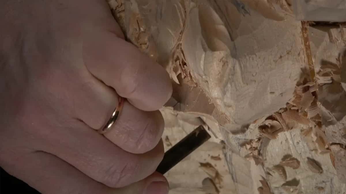 Fingers press a flat gouge into the wood