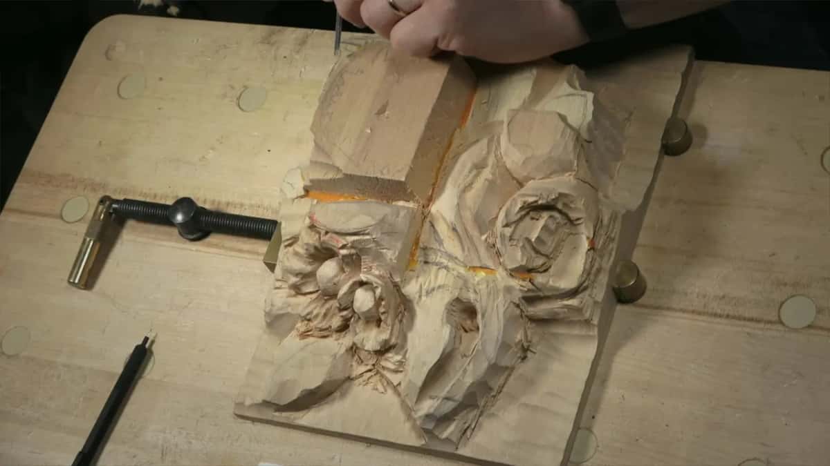 From above, fingers press a narrow tool into one corner of the tall block, a screw clamp beside it