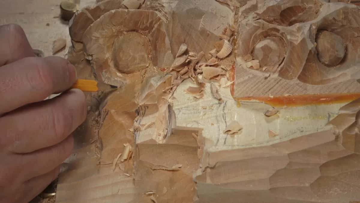 A pencil in his fingers draws fresh lines across the top block, curled chips around it