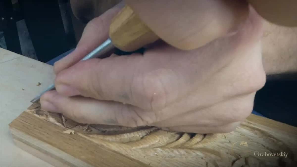 Right hand drives a small tool along a long carved leaf