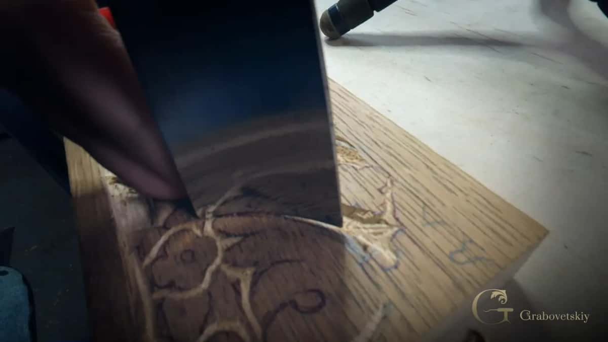 A wide gouge blade sits in a curve beside a flower outline on the oak