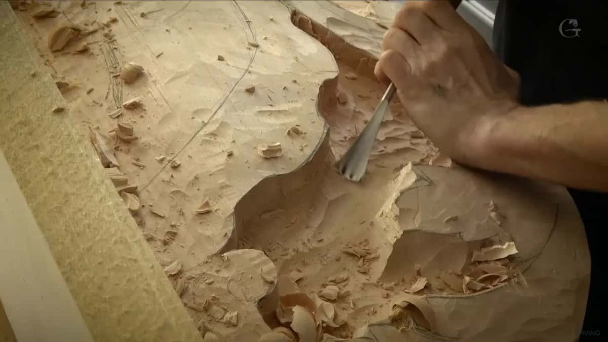A gouge pushed into the deep waste of a big carving, chips piled all around it