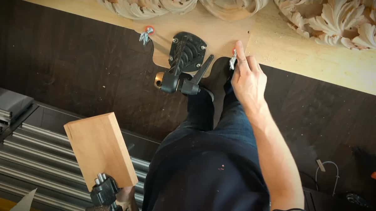 Seen from above, a man stands at a plywood board held down by small clamps