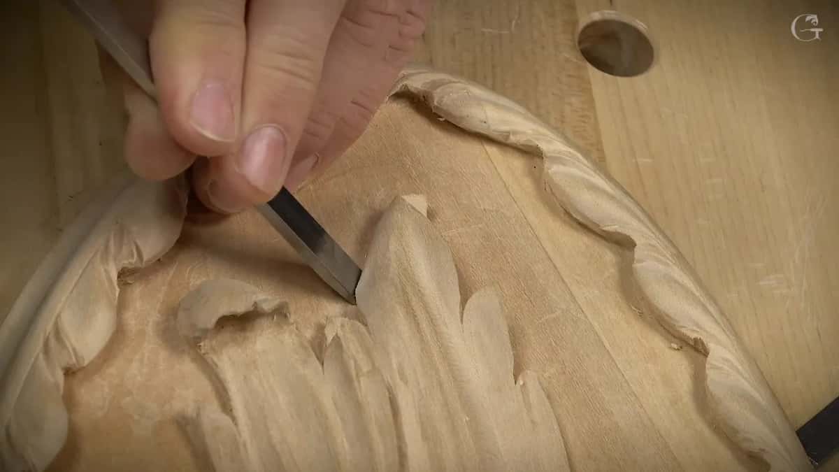 A slim metal tool angled into the corner at the base of a carved leaf tip.