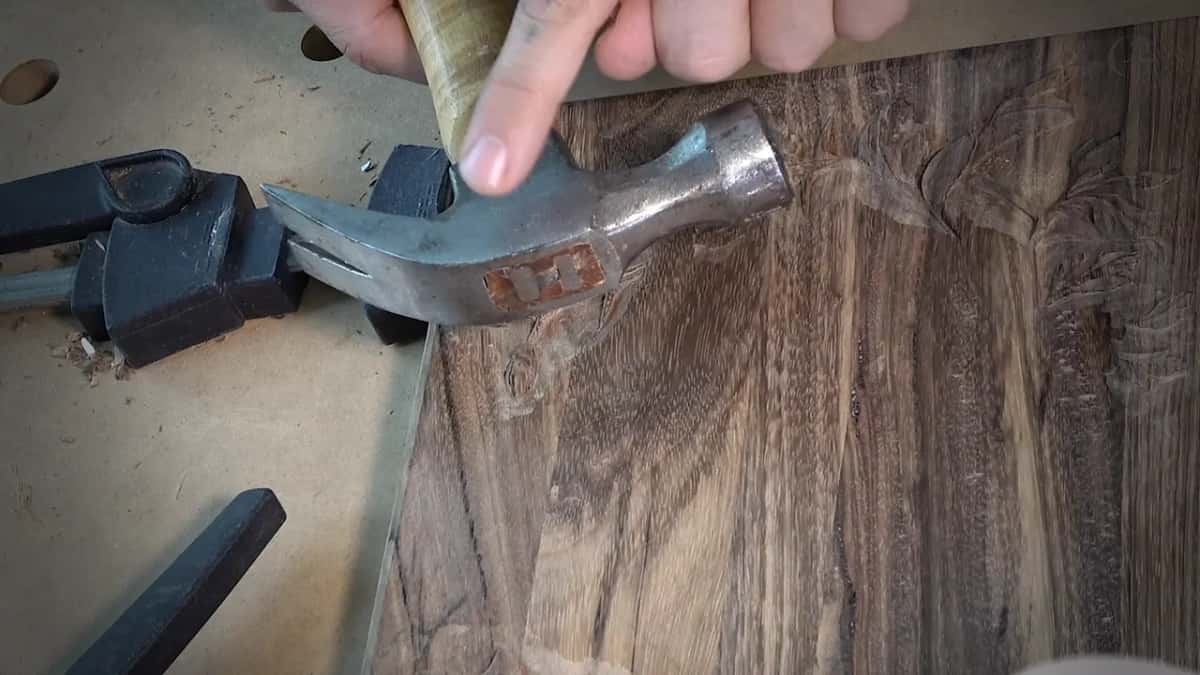 A claw hammer turned on its side over a dark board with shallow carving.