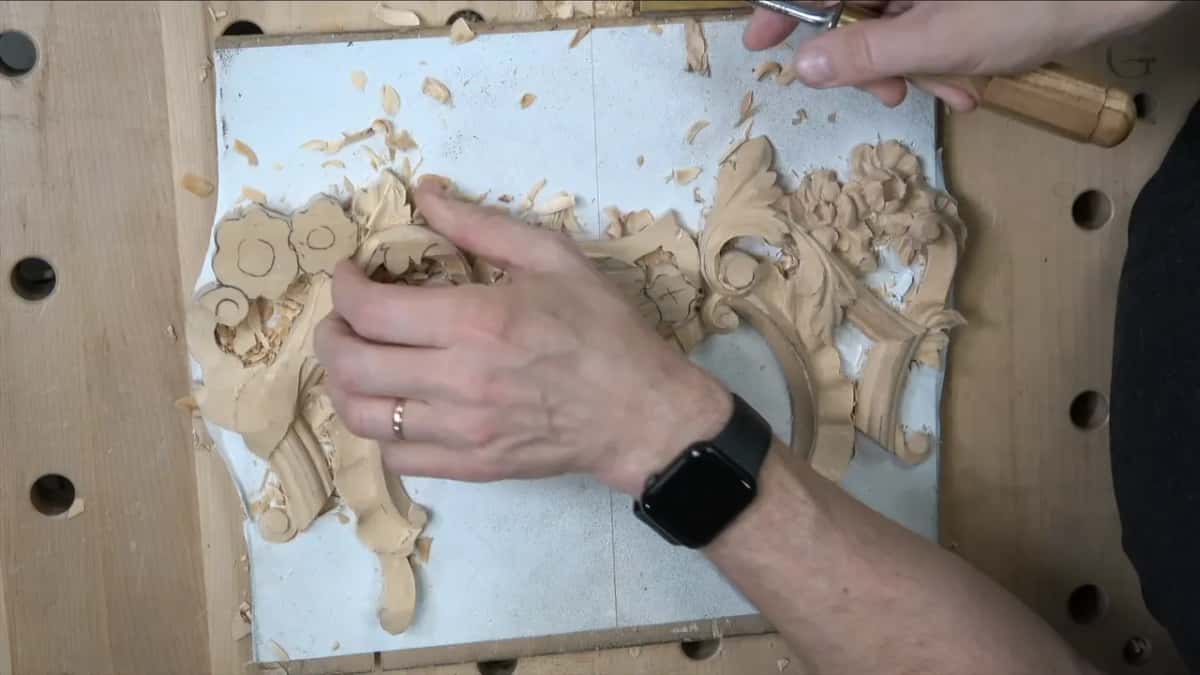 Gouge in hand over a leafy carving