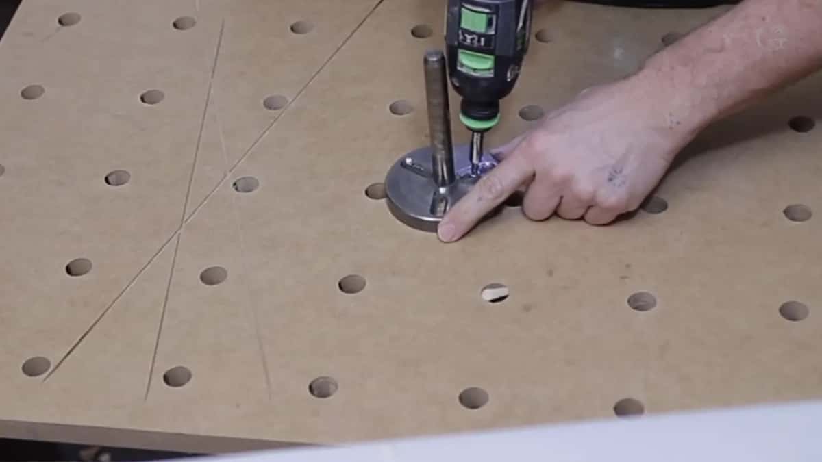 A cordless driver at a round metal plate on a holed MDF board