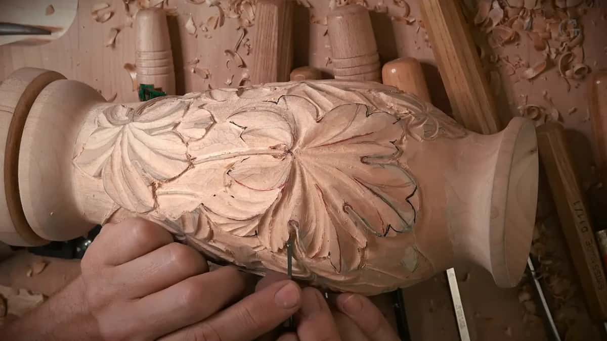 With the vase lying in the vise, a narrow gouge notches the edge of one leaf division