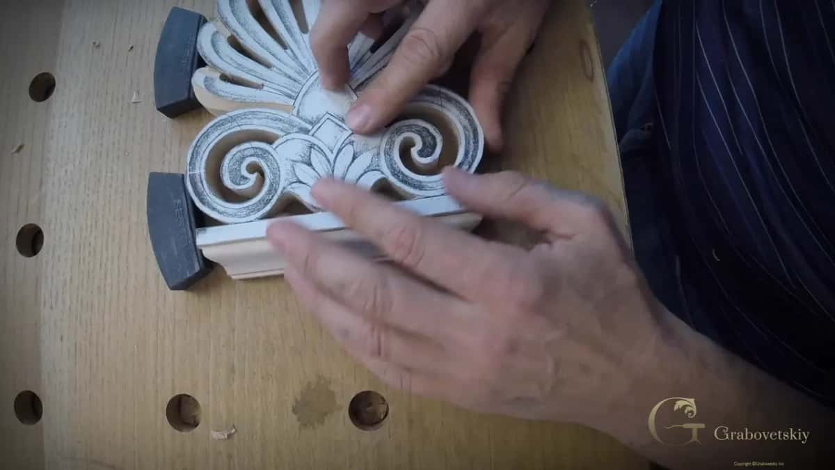 Fingers spread across the palmette scrolls while two black stops hold its lower edge on a holed oak bench.