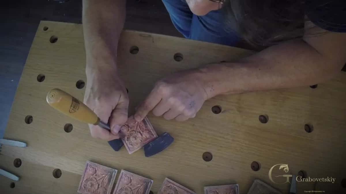 A yellow handled gouge works a small rosette block held by two dark stops, finished blocks below.