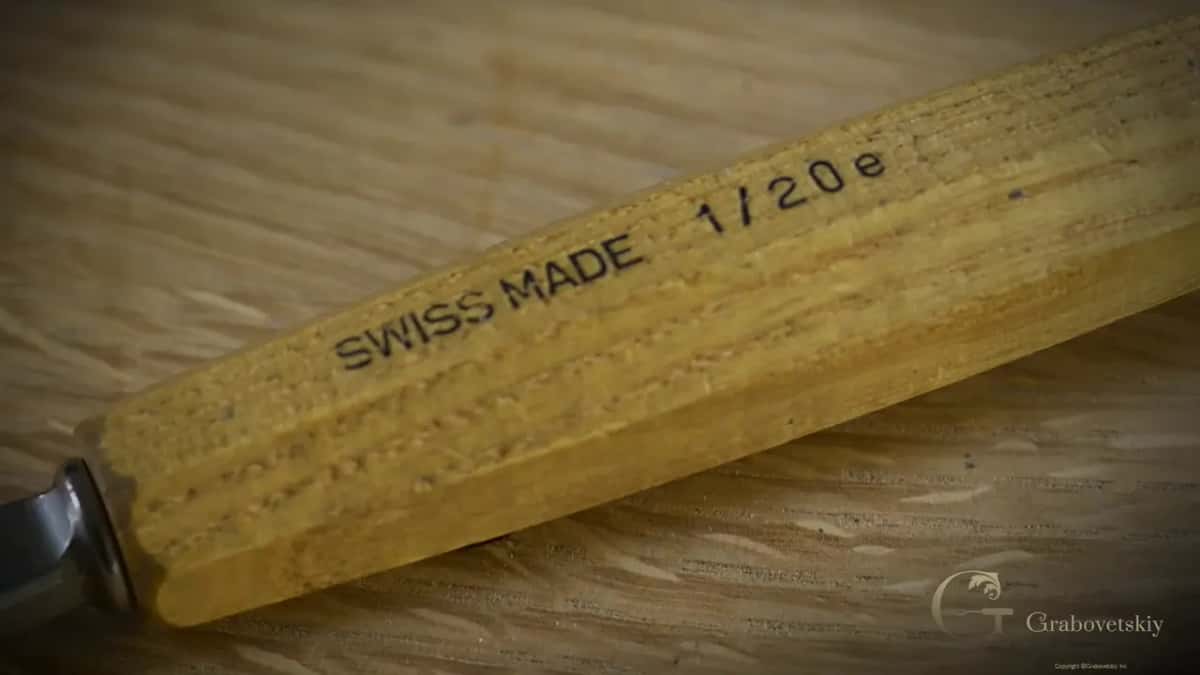 A tool handle stamped Swiss Made and 1/20e lies on the light oak bench.