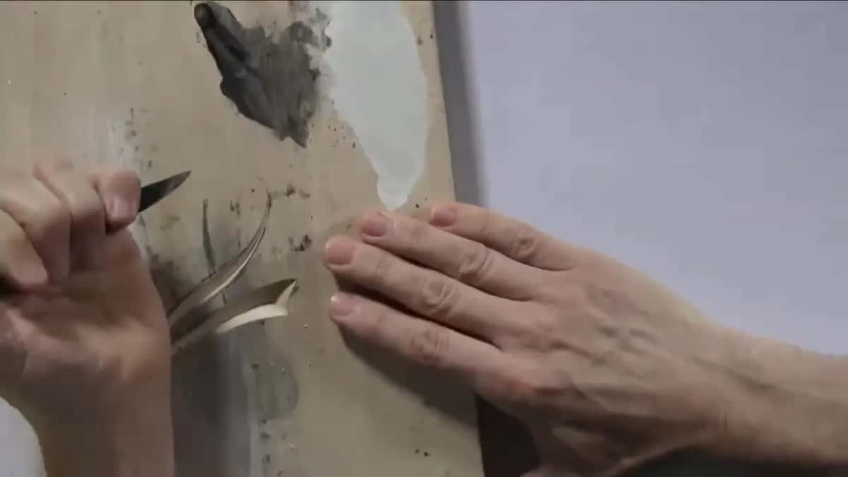 Knife held low in one fist while the other hand lies flat on the board beside the letter