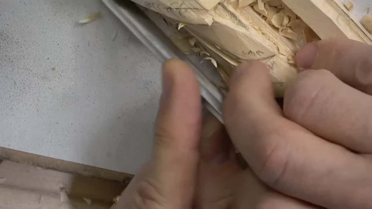Fingertips pinching a small gouge close to its edge as it runs along the molding