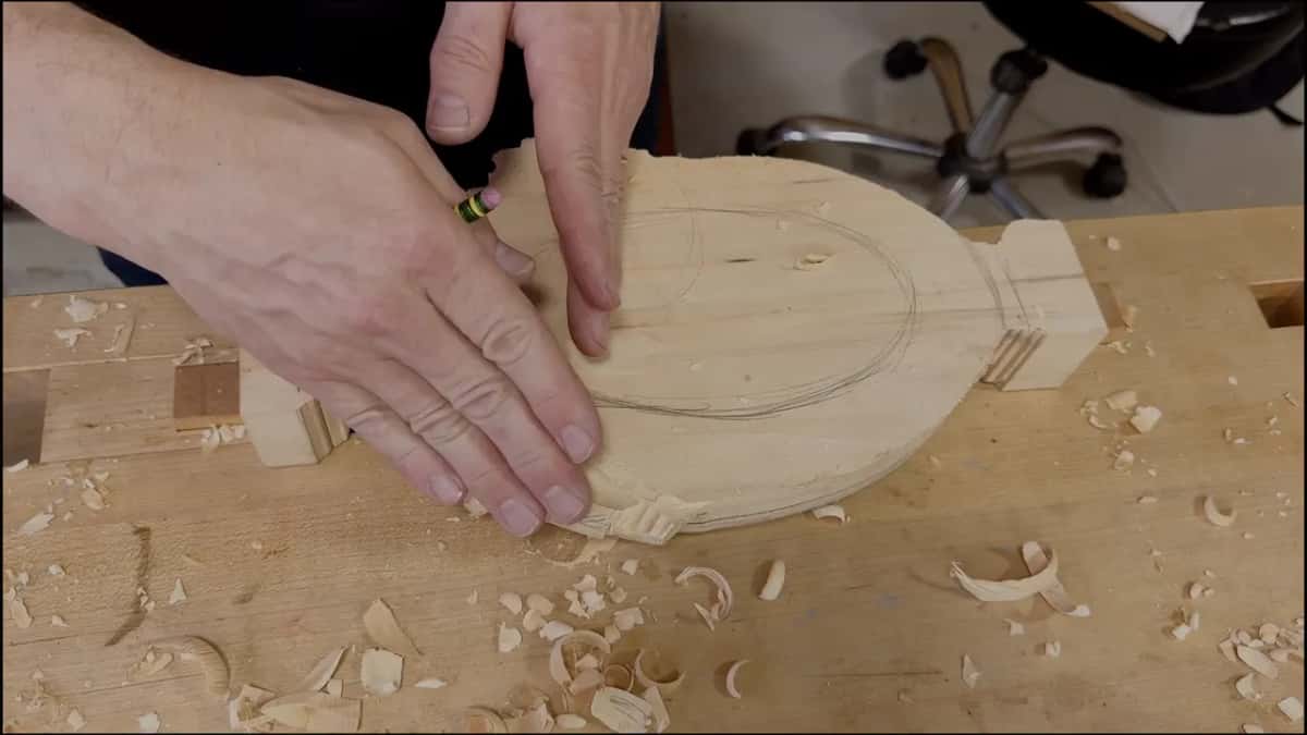 Two hands on an oval tray blank, a pencil oval drawn inside it, shavings on the bench
