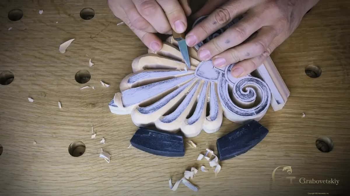 Knife held in both hands, carving into the center of a palm fan ringed by chips