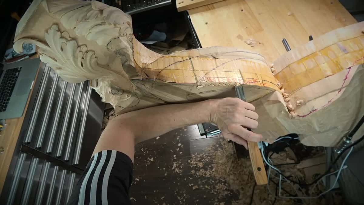 Stacked layers run along the side of a big carving while one hand pushes a gouge near red lines