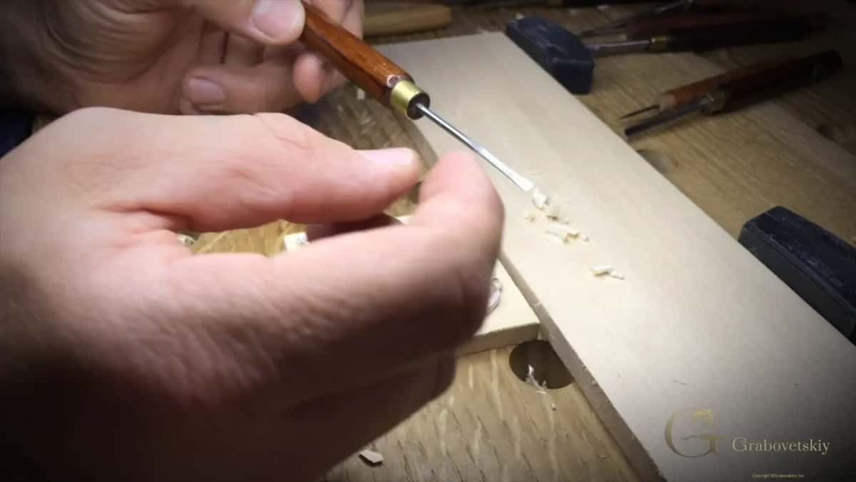 Small gouge with a red handle and a brass ferrule working the ground next to the strip of spare wood.