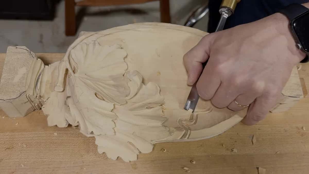 Seen from above, the whole tray with one hand holding a gouge close to the drawn curl near the leaf
