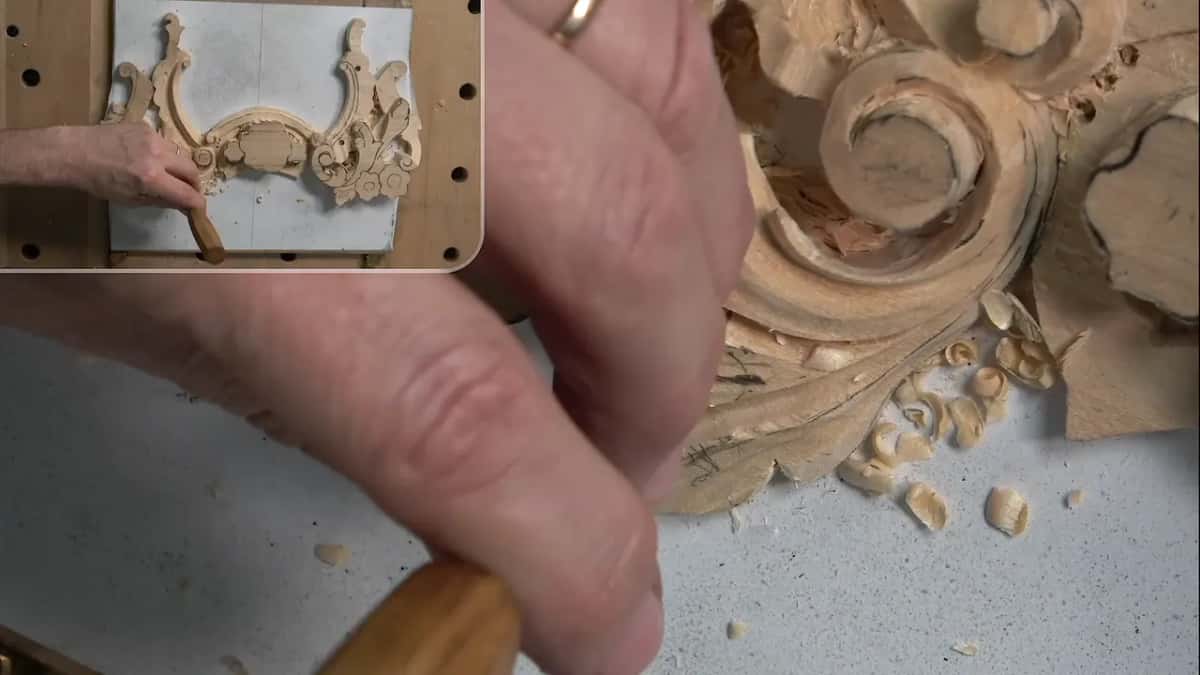 Big fingers around a handle, acanthus scrolls behind, a small inset of the whole panel in the corner