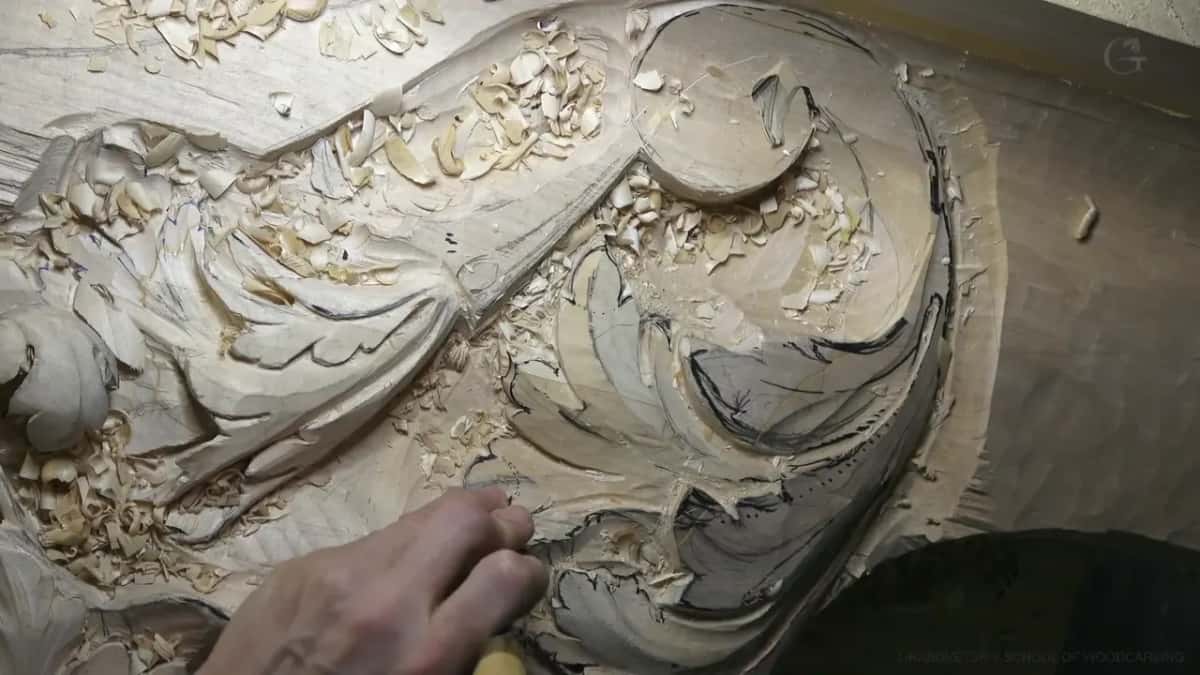 Fingertips working at the curl of a carved scroll, loose chips scattered all around them