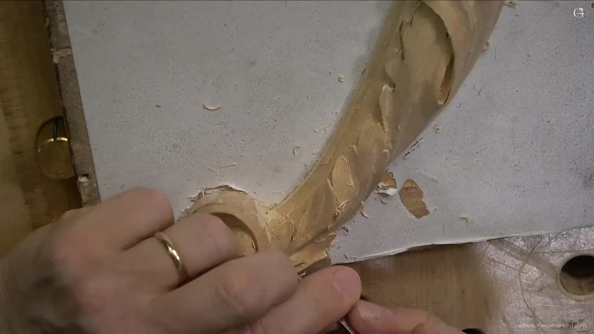 A ringed hand works on a leaf where it crosses the molding, with chips on a gray board