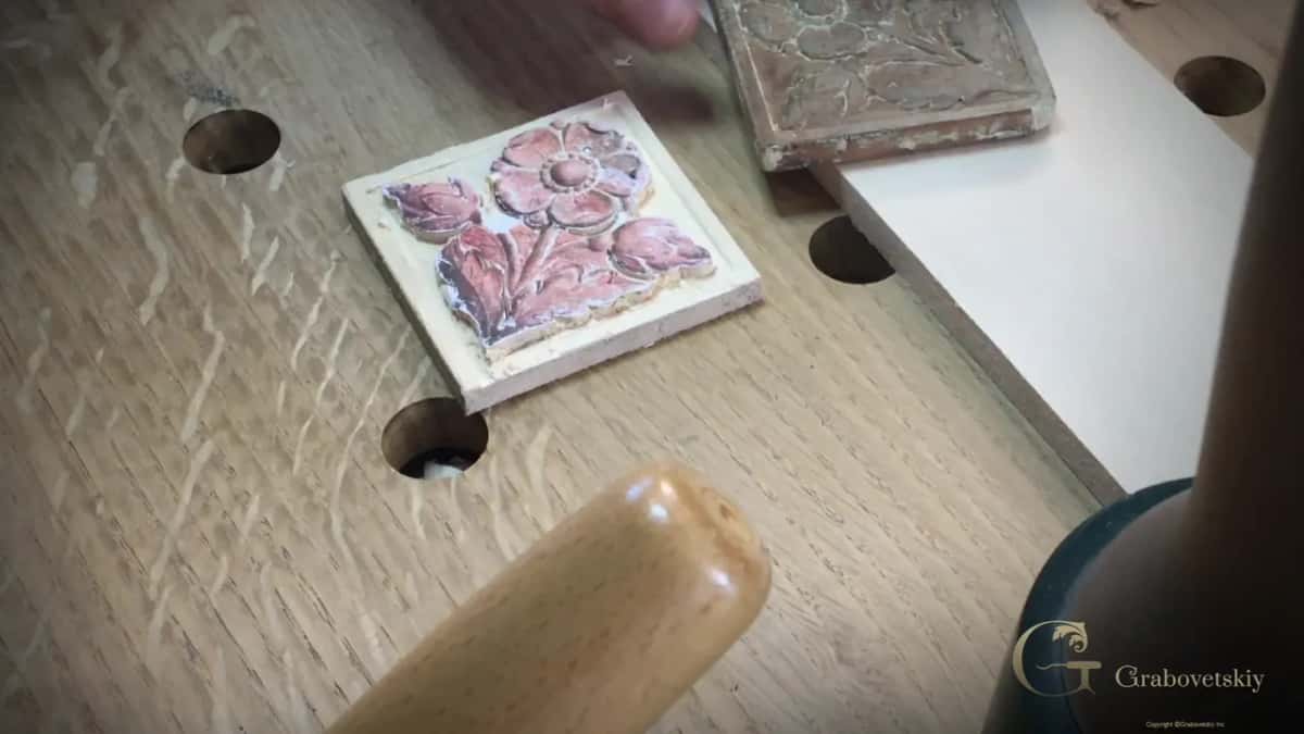 Half-carved copy up front with the dark original behind it and a mallet handle at the bottom edge