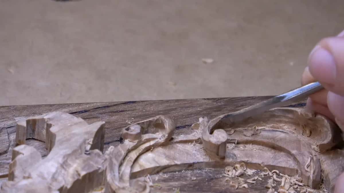 Chips lie on the ground of the scroll as a gouge pushes along the inside of its curve.
