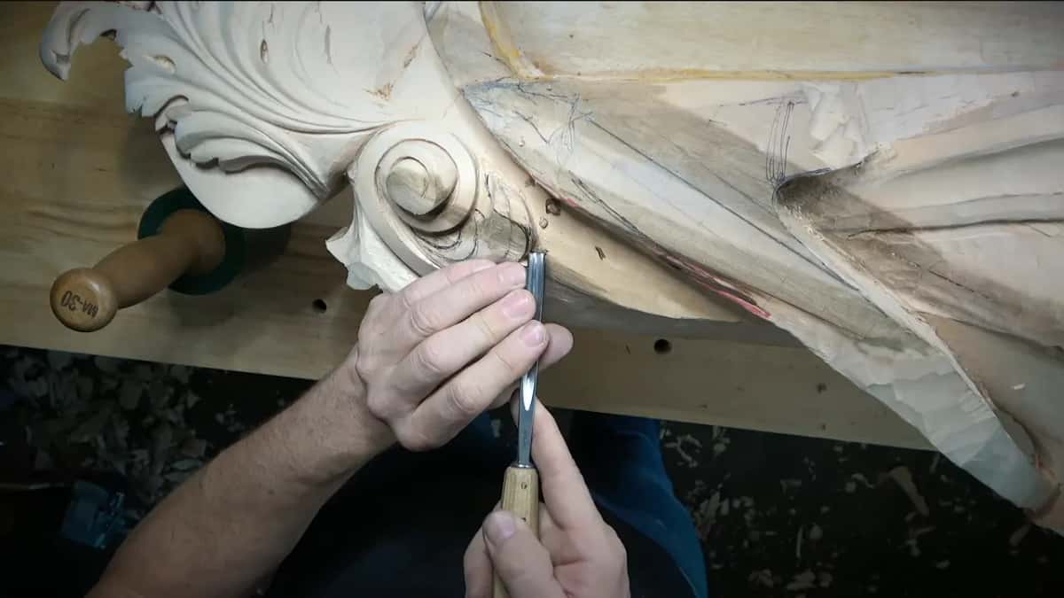 Both hands steady a gouge under a big volute.