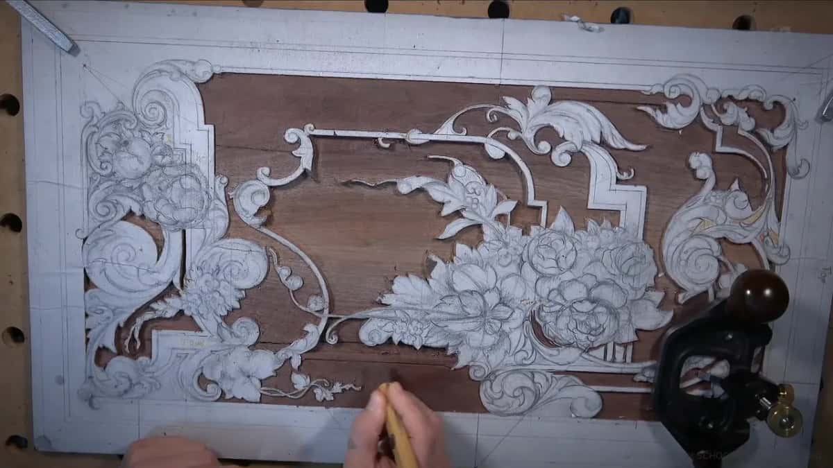 Gray pattern of scrolls and flowers over a dark board, a black tool and a pencil near the bottom