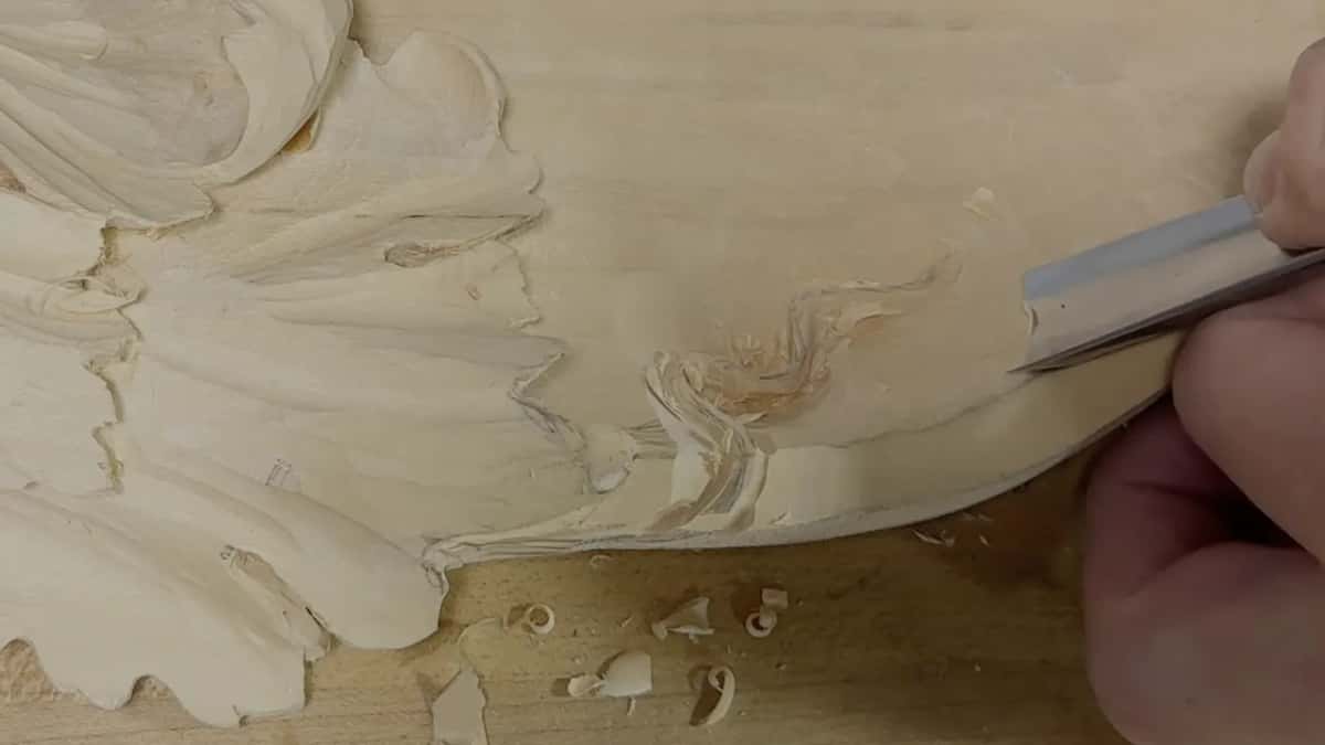 Flat gouge shaving the bowl's edge beside a small curl of tendril, close to the lowest lobes of the leaf