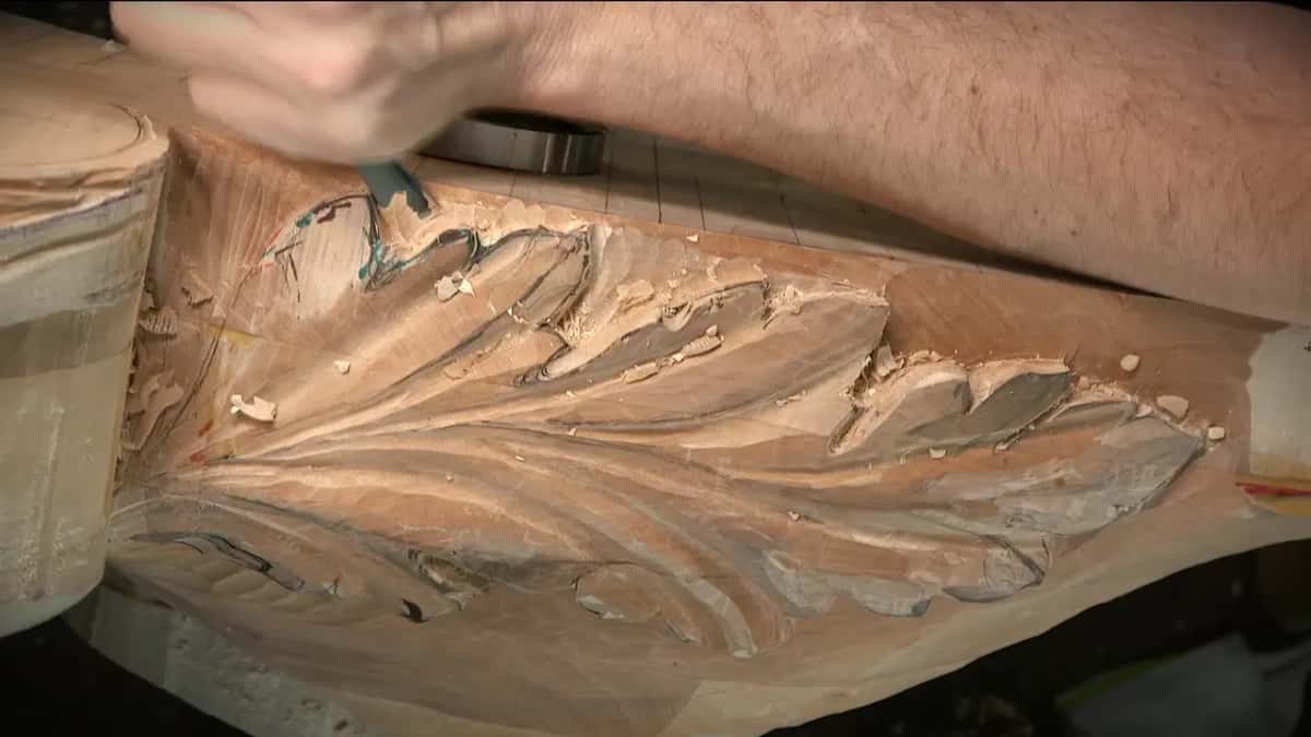 Acanthus along the side of a long curved piece, one hand working a gouge into a lobe
